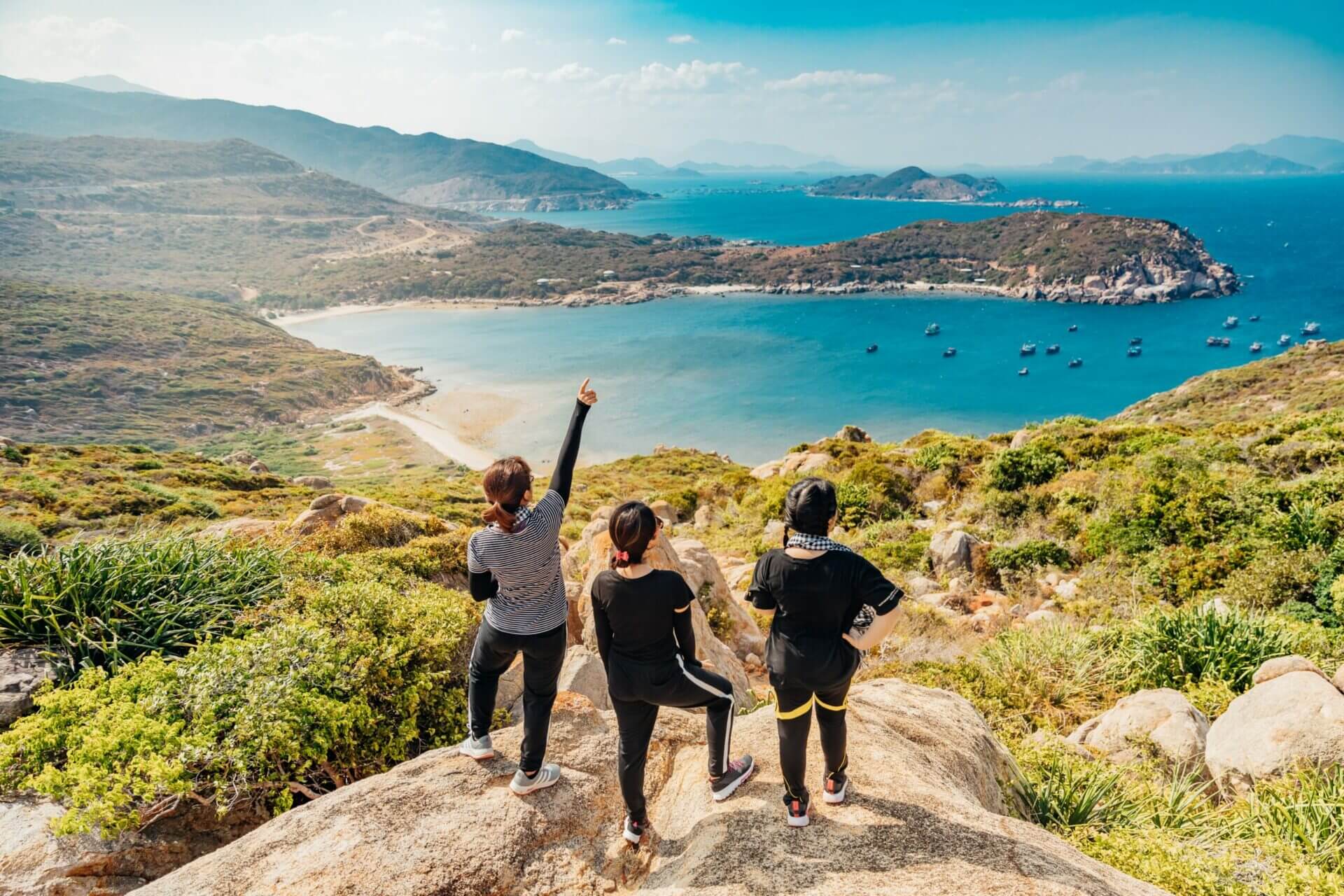 three people standing on a mountain looking at the sea